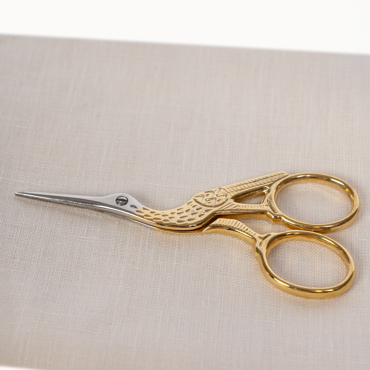 Gold bird-shaped scissors with silver metal blades, resting on a light beige textured fabric background.