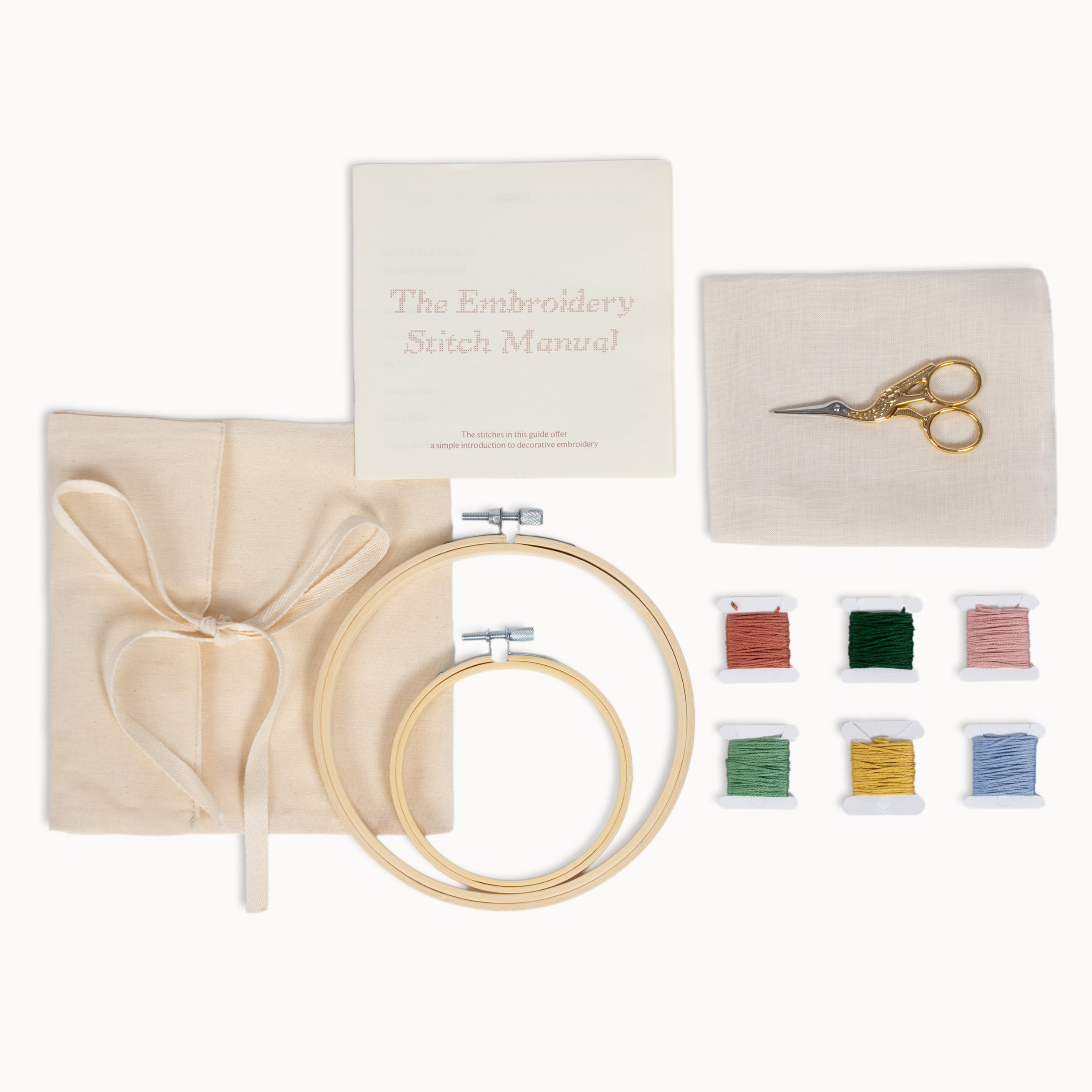 Embroidery kit laid out on a white background, including a wooden hoop, fabric, scissors, a small booklet titled 'The Embroidery Stitch Manual,' and six spools of thread in red, green, pink, yellow, blue, and light blue.