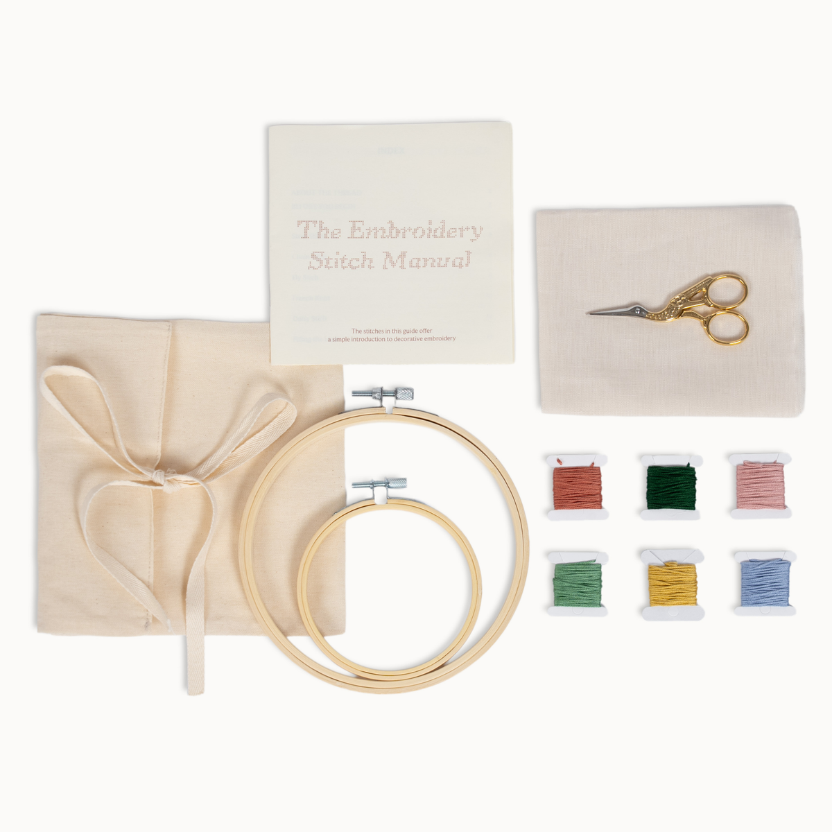 Embroidery kit laid out on a white background, including a wooden hoop, fabric, scissors, a small booklet titled 'The Embroidery Stitch Manual,' and six spools of thread in red, green, pink, yellow, blue, and light blue.