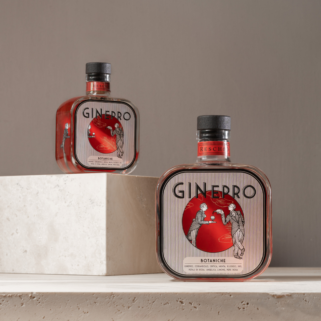 Two Ginepro Botaniche gin bottles with a distinctive square shape and black caps, styled on a white shelf with a beige background.