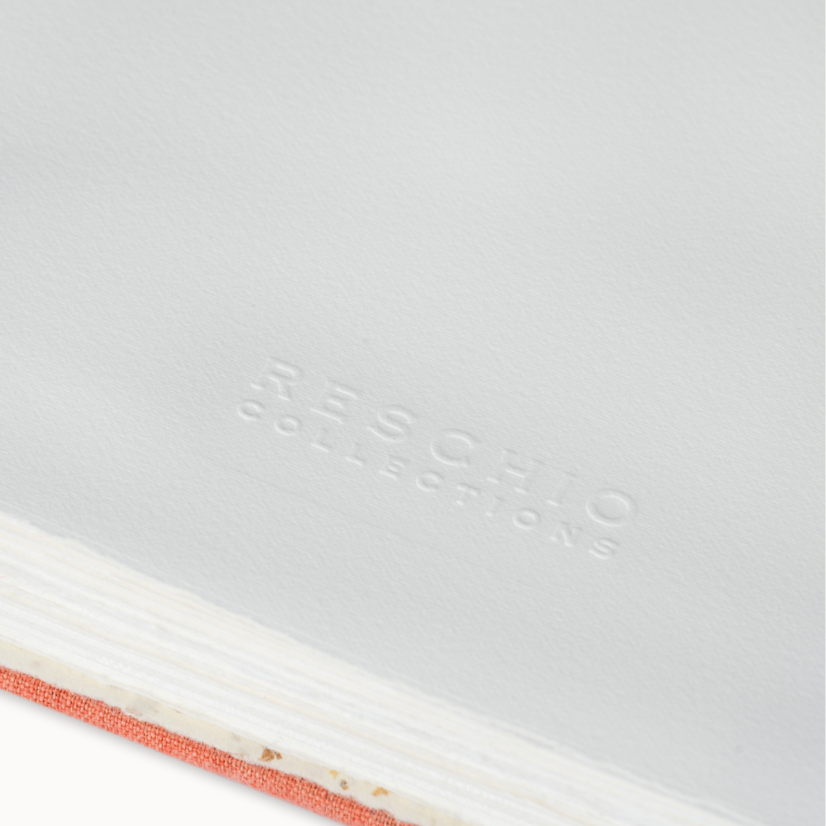 Close-up of a white notebook or book cover with embossed 'RESCHIO COLLECTIONS' text and a coral-pink textured edge visible along the bottom left.