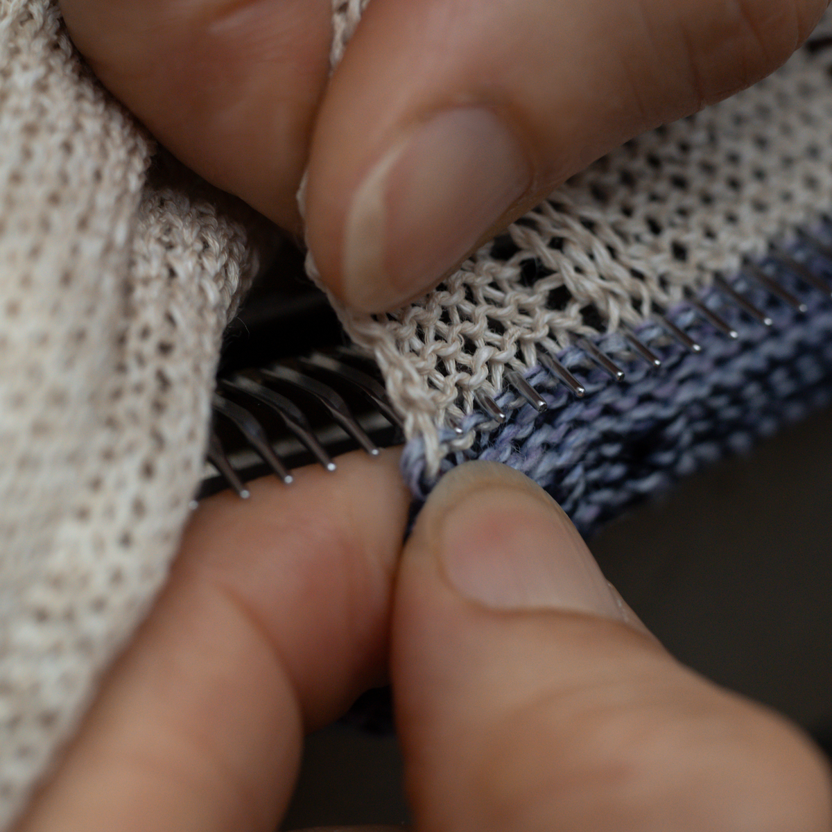 Close-up of a person's fingers holding open a zippered textile item, showing the cream knit fabric, blue knit fabric, and metal zipper teeth.