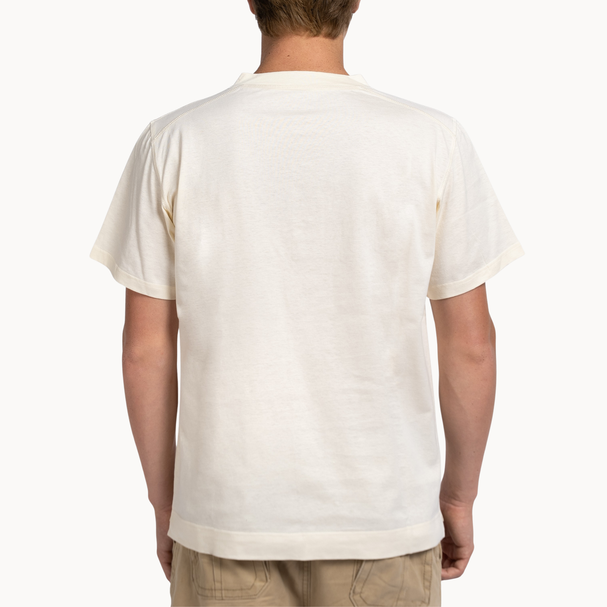 A man viewed from the back wearing a short-sleeve crewneck t-shirt in off-white/cream, paired with khaki pants, against a plain white background.