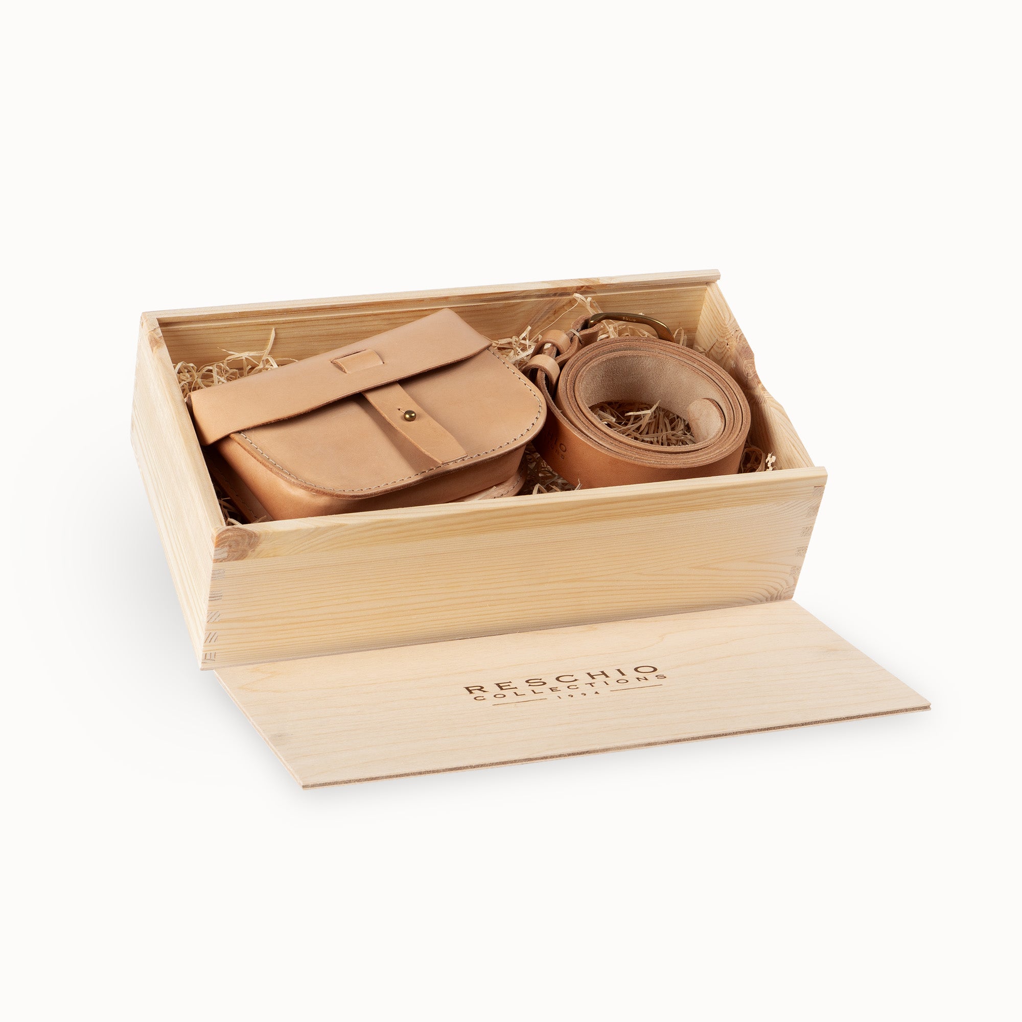 A tan leather shoulder bag with a matching rolled strap, presented inside a light wood gift box with a branded lid on a white background.