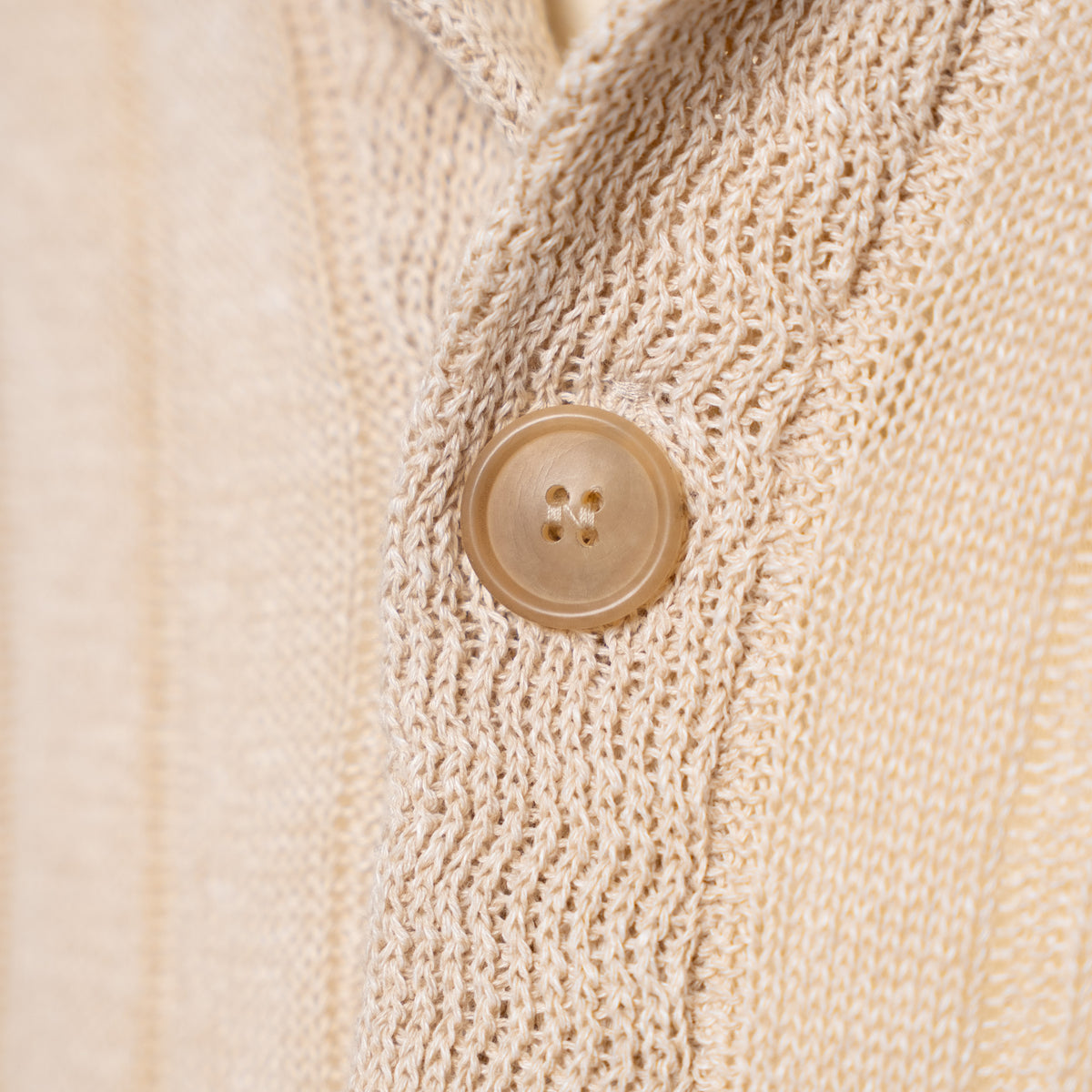 Close-up of a cream-colored knit cardigan sweater showing the detailed knit texture and a matching four-hole button.
