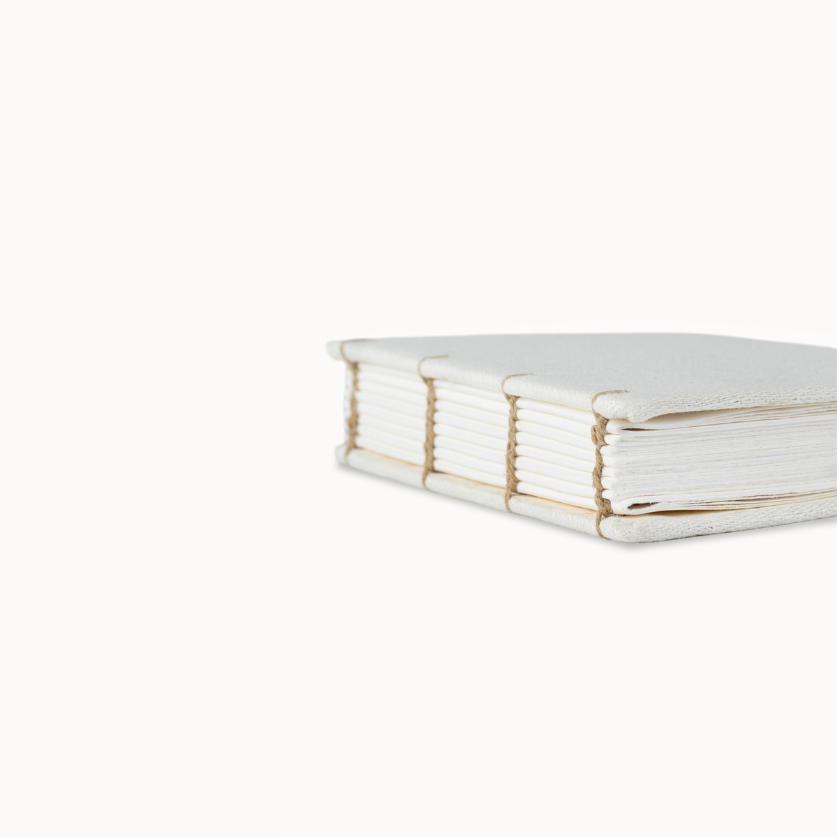 A close-up side view of a white hardcover book or journal with visible page edges and tan binding cords, photographed on a clean white background.