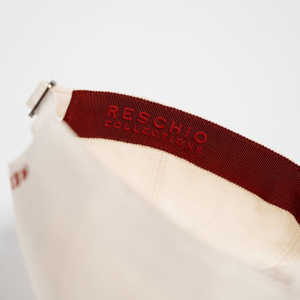 Close-up of a white cap with a red elastic band displaying the brand name 'RESCHIO COLLECTIONS' in red embroidery.