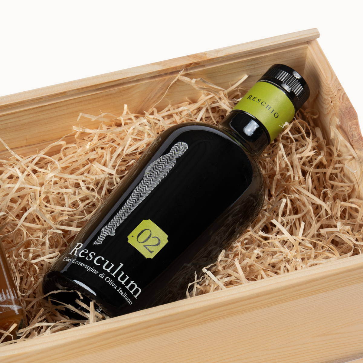 A dark glass bottle labeled 'Reseclum 02' resting on shredded paper inside a light wood box.