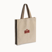A natural beige canvas tote bag with dark brown handles and a small red printed graphic on the front, shown on a clean white background.