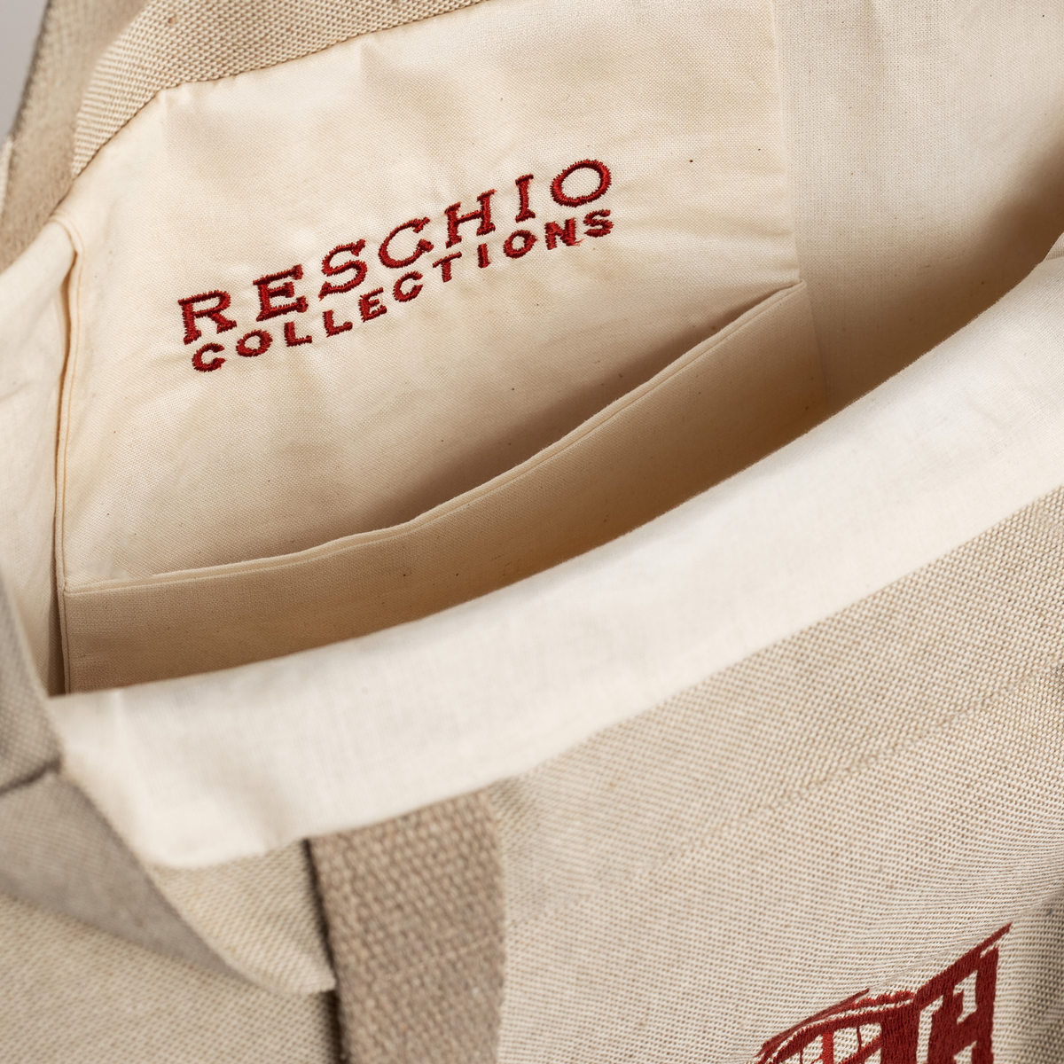 Close-up of a beige canvas tote bag showing the interior lining with 'RESCHIO COLLECTIONS' printed in red inside a side pocket.
