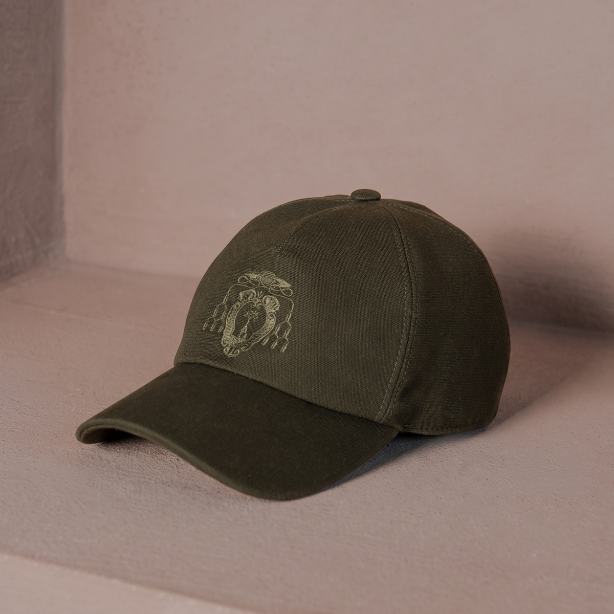An olive green baseball cap with a tonal embroidered lion crest on the front, displayed on a textured beige surface.