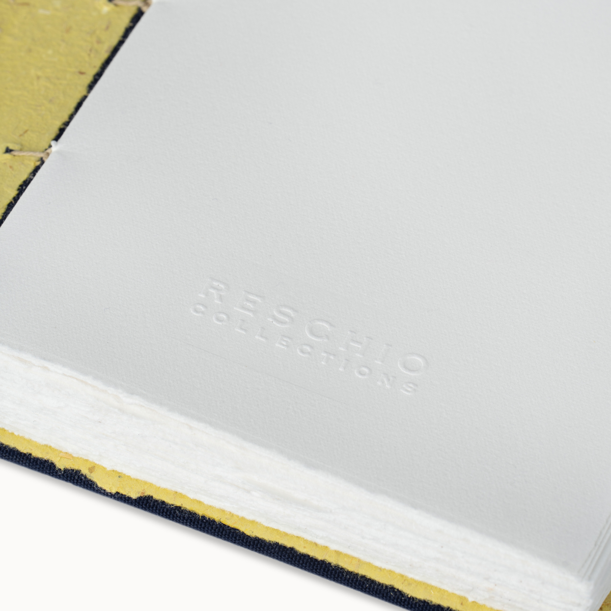 A close-up of a white hardcover notebook or journal with the debossed brand name 'RESCHIO COLLECTIONS' on the cover, showing a textured yellow-gold inner page and dark navy fabric binding edge.